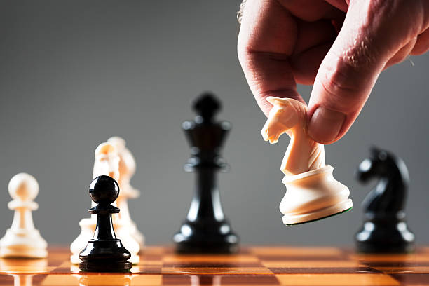 mans-hand-moves-white-knight-into-position-on-chessboard-picture-id134955466