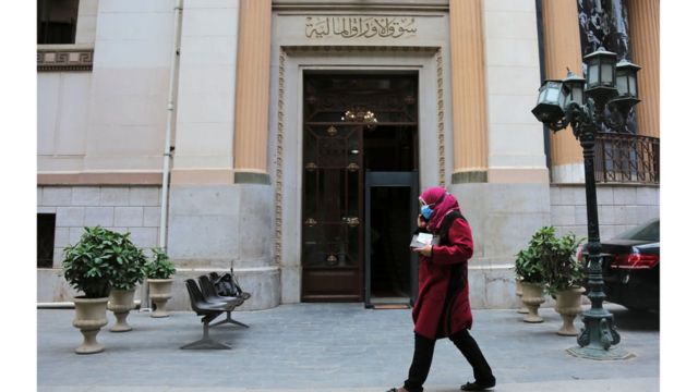 صورة لسيدة تسير أمام مقر البورصة المصرية وترتدي قناعا، وسط أزمة وباء كورونا عام 2020