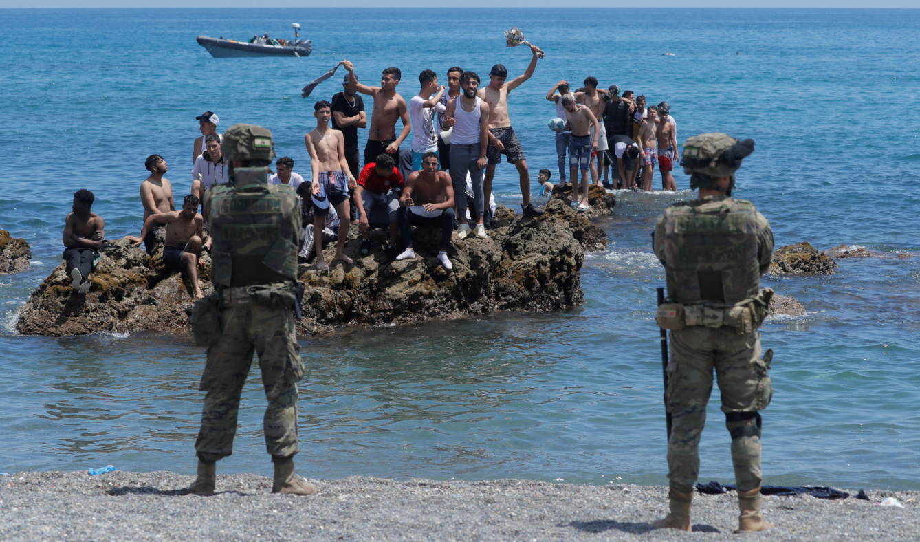 جنديان من الجيش الإسباني أمام بعض الشباب المغربي الذين سبحوا إلى سبتة.  (رويترز)